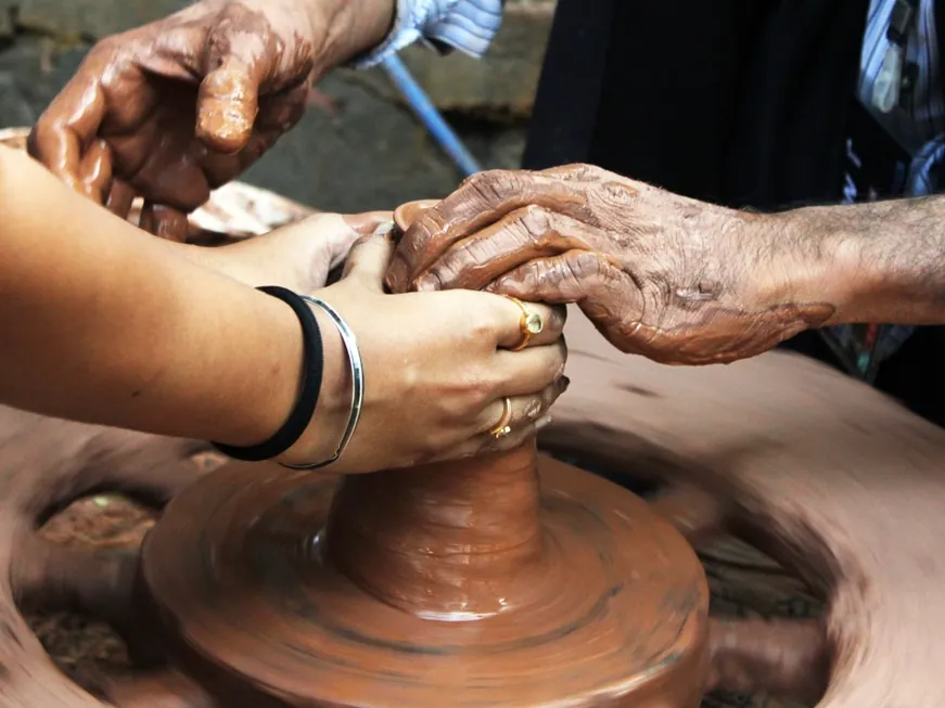 Two people's hands shaping clay together on a potter's wheel