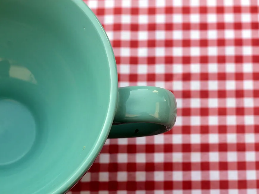 A mint-green handmade mug on a gingham tablecloth