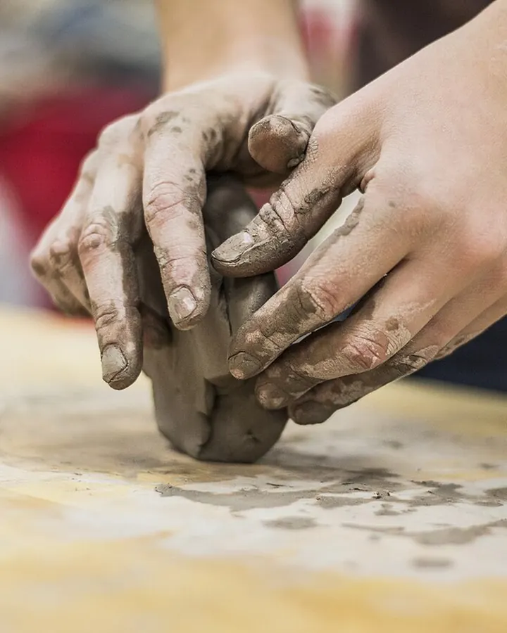 Hands wedging a fresh block of clay on a worktable